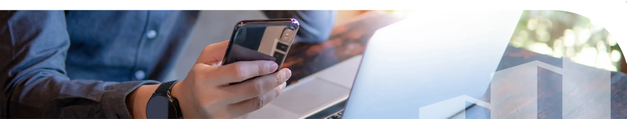 A man looking at a phone sitting in front of a laptop.